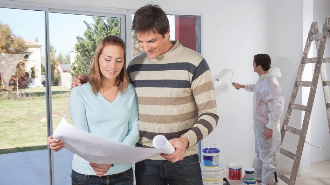 Couple going through house plan while painter in the background