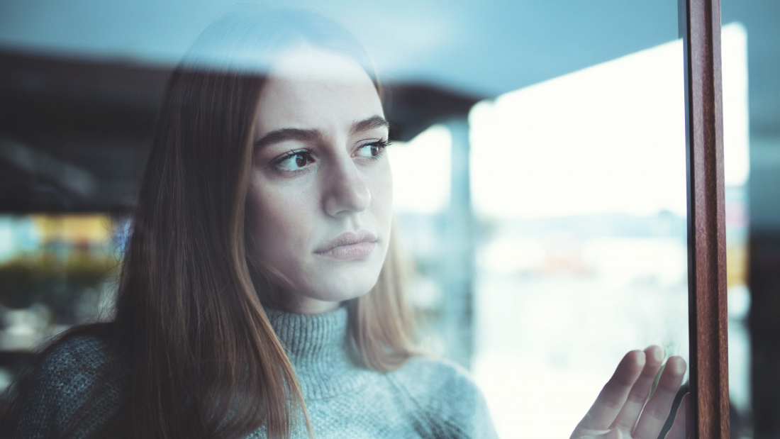 Causian sad lonely young woman looking thoughtfully through the window during pandemic, and celebrating christmas alone, shot with canon 5dsr