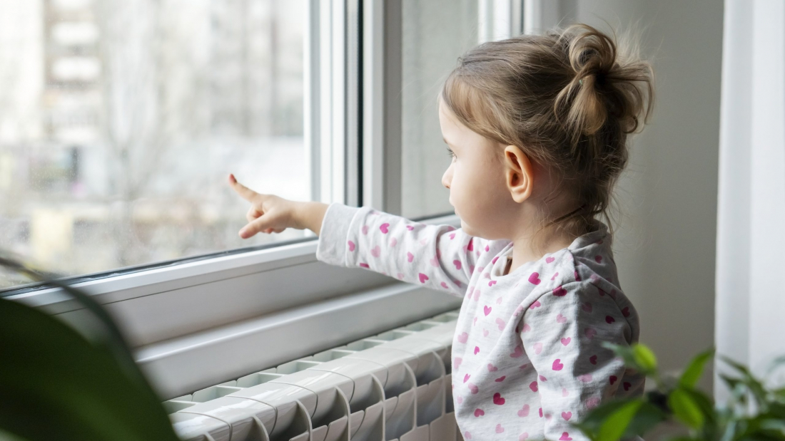 Little girl standing and looking through the window while her mother packing the moving boxes.