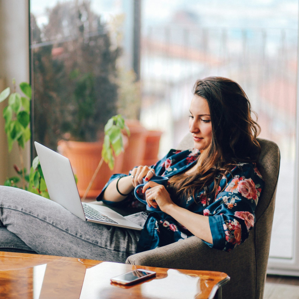 Vintage toned portrait of a young woman working at the table in the bright and beautiful apartment on the high floor in Belgrade, Serbia. She is wearing casual, everyday clothes and having a cup of coffee as well.